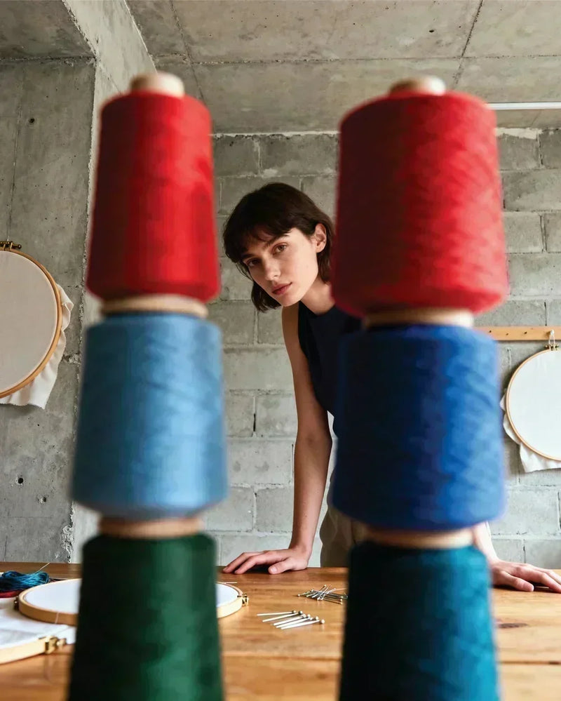 Fashion designer reviewing colorful thread spools in a clothing studio while planning garment production and apparel manufacturing.