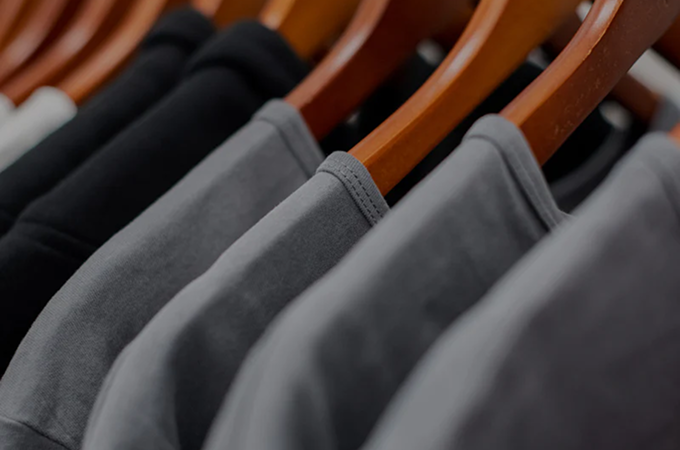 A close-up of black and grey t-shirts hanging on wooden hangers at In-House, Canada.