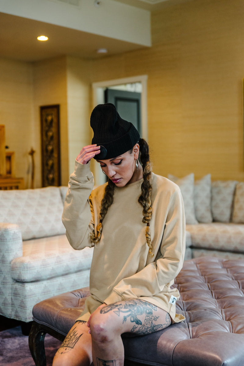 Model wearing an oversized beige In-House long-sleeve t-shirt, styled with a black beanie and braids for a streetwear look.