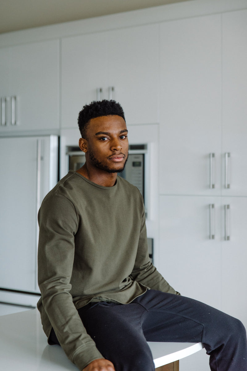A model wearing an In-House custom t-shirt with jeans, sitting on a white table in a minimalist setting.
